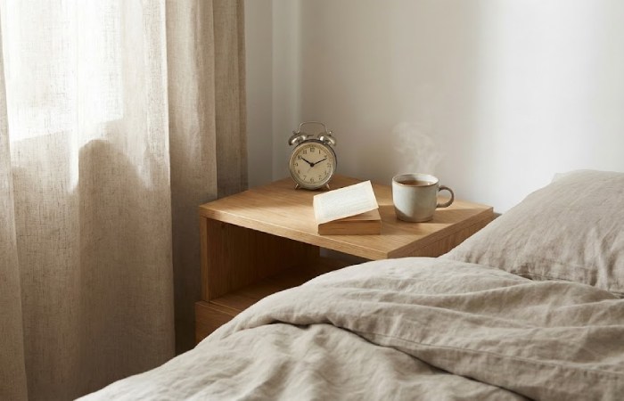 Warm minimalist nightstand with an analog alarm clock and book, illustrating a phone-free morning routine.